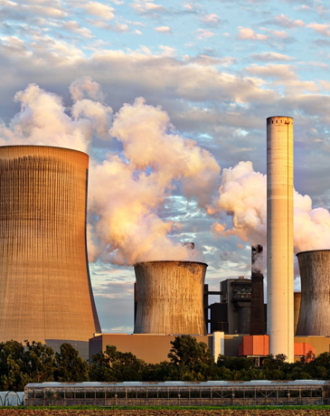 Cooling towers and chimney stack of an industrial power plant emitting steam.