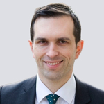 Professional headshot of a smiling man wearing a dark suit and patterned tie.
