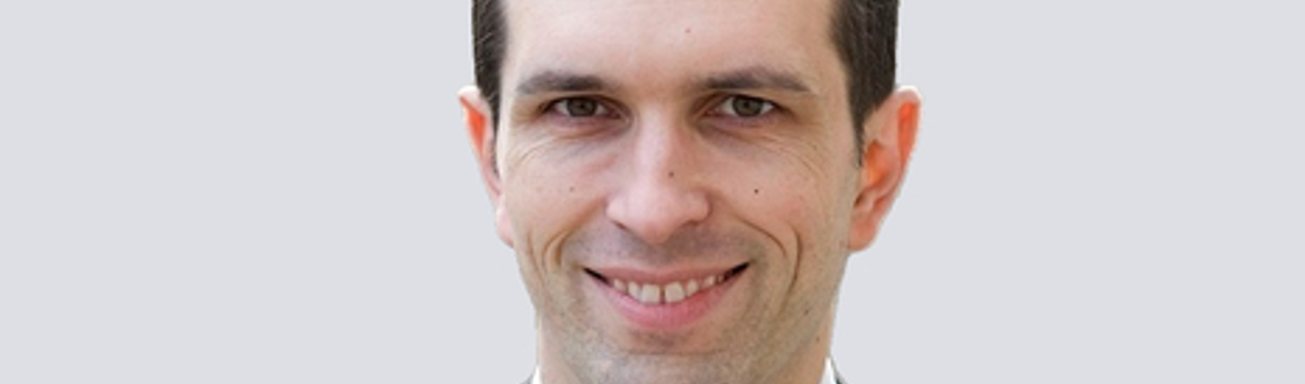 Professional headshot of a smiling man wearing a dark suit and patterned tie.
