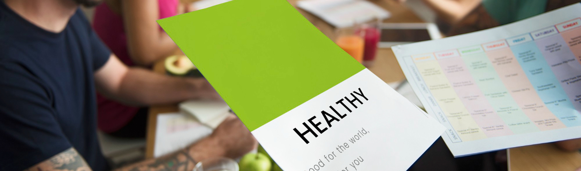 People at a meeting table reviewing a document titled "HEALTHY" and a colourful weekly planner.