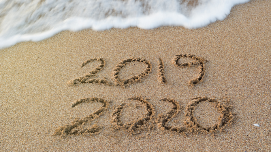 A wave washing away the number "2020" which has been written in the sand. Leaving only 2020 in the sand