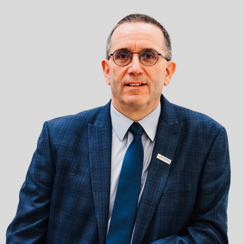 Headshot of a man wearing a blue checked suit, blue tie, and round glasses.
