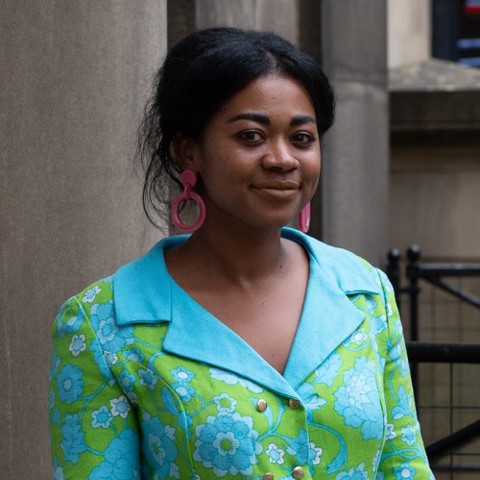 Woman wearing a bright green floral jacket, blue collar, and large pink earrings.