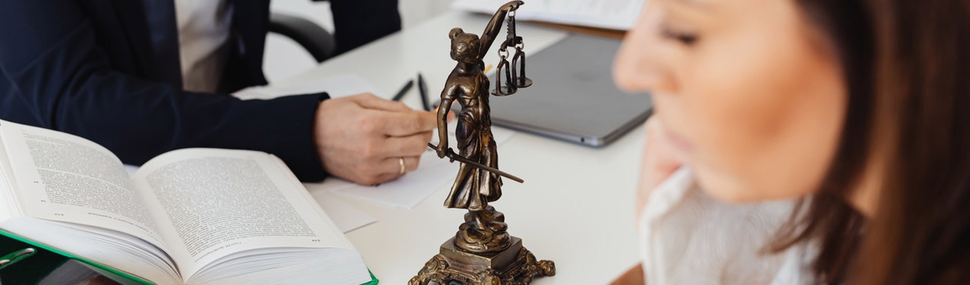 Bronze Lady Justice statue on a desk during a meeting between a solicitor and a client.
