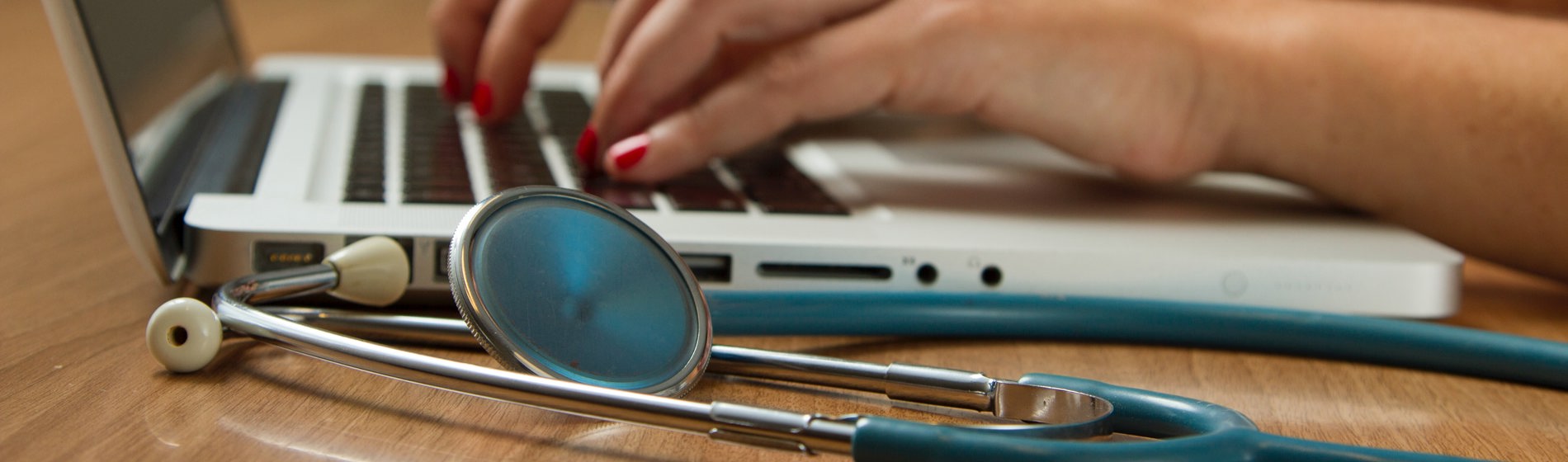 Close-up of a stethoscope and hands typing on a laptop.