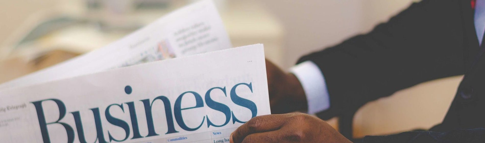 A professional in a suit reads a newspaper titled 'Business'.