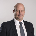 Professional portrait of a bald man in a dark suit and grey tie.