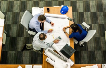 Three professionals review architectural blueprints and plans on a desk, suggesting collaboration.