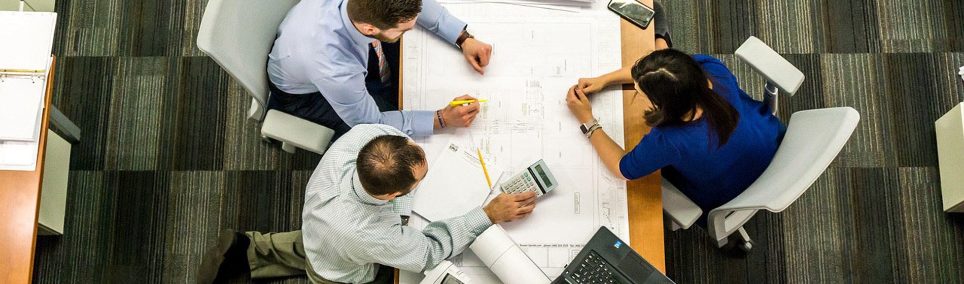 Three professionals review architectural blueprints and plans on a desk, suggesting collaboration.
