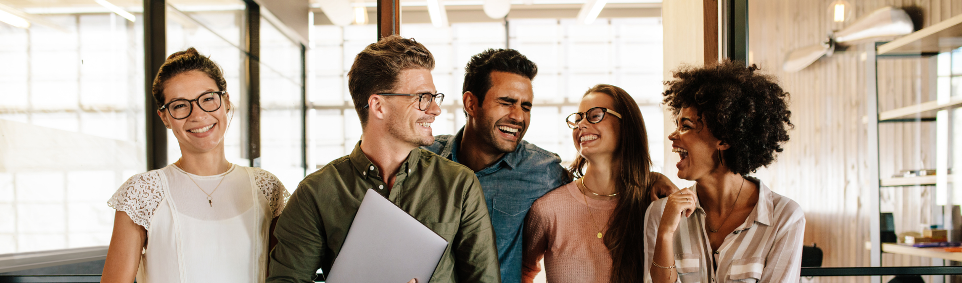Diverse group of five professionals smiling and laughing together in a bright, modern office.