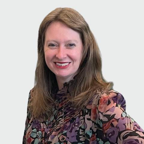 A smiling woman with long brown hair wearing a colourful floral blouse.