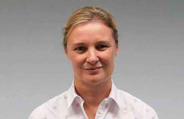 Blonde woman in a white patterned shirt, professional headshot.