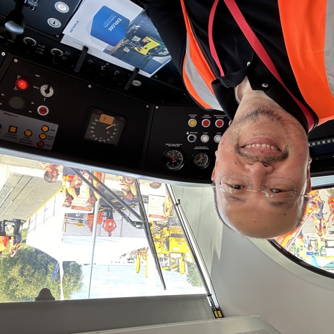 Smiling man in a high-vis vest sits in a train cab, looking out at an industry event.