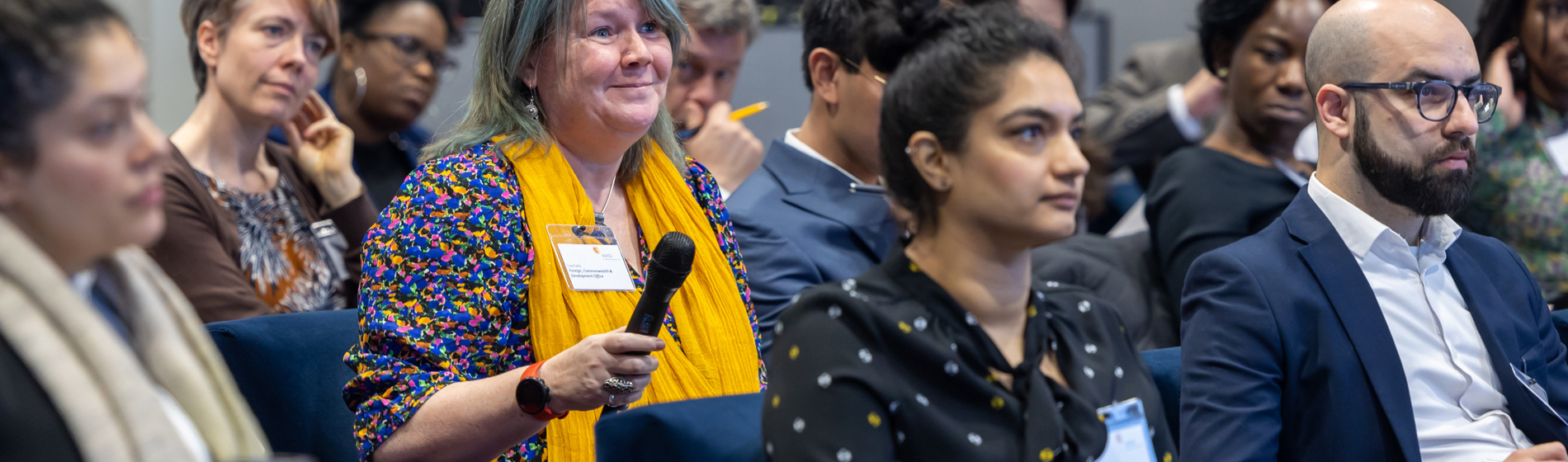 A smiling woman holds a microphone while participating in a conference Q&A session.