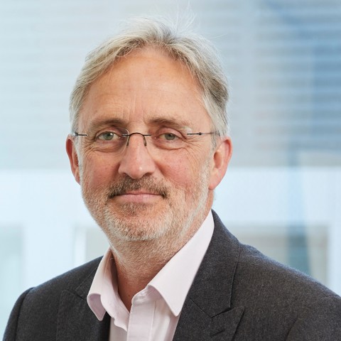 Professional headshot of a smiling man with grey hair, beard, and glasses.